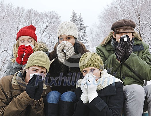Group of diverse young friends blowing noses outdoors in winter Group of diverse young friends blowing noses outdoors in winter