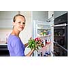 Pretty, young woman taking fresh vegetables from her fridge - being on a gluten free vegan diet does not seem to be a problem for her (shallow DOF; color toned image)