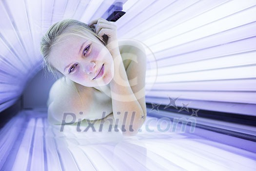 Pretty, young woman tanning her skin in a modern solarium (shallow DOF; color toned image)