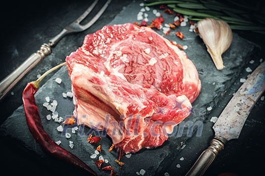 Raw beef steak with salt and herbs on stone cutting board. Vintage toned. Raw beef steak with salt and herbs on stone cutting board. Vintage toned.