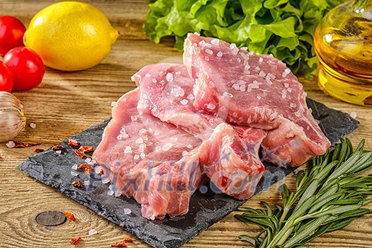 Raw pork steaks on stone board with herbs, tomatoes, garlic and lemon Raw pork steaks on stone board with herbs, tomatoes, garlic and lemon