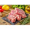 Raw pork steaks on stone board with herbs, tomatoes, garlic and lemon