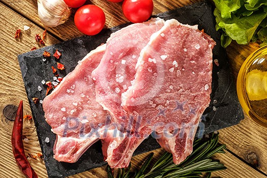 Raw pork steaks on stone board with herbs, tomatoes, garlic and lemon Raw pork steaks on stone board with herbs, tomatoes, garlic and lemon