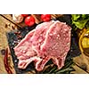 Raw pork steaks on stone board with herbs, tomatoes, garlic and lemon