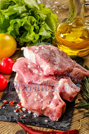 Raw pork steaks on stone board with herbs, tomatoes and lemon