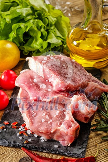Raw pork steaks on stone board with herbs, tomatoes and lemon Raw pork steaks on stone board with herbs, tomatoes and lemon