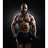 Strong bodybuilder with six pack, perfect abs, shoulders, biceps, triceps and chest. Power athletic bearded man in training pumping up muscles with dumbbell.