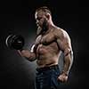 Strong bodybuilder with six pack, perfect abs, shoulders, biceps, triceps and chest. Power athletic bearded man in training pumping up muscles with dumbbell.