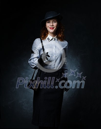 Red-haired girl in retro dress on a dark background. A long skirt and a dark hat. Keeps bag on his shoulder.