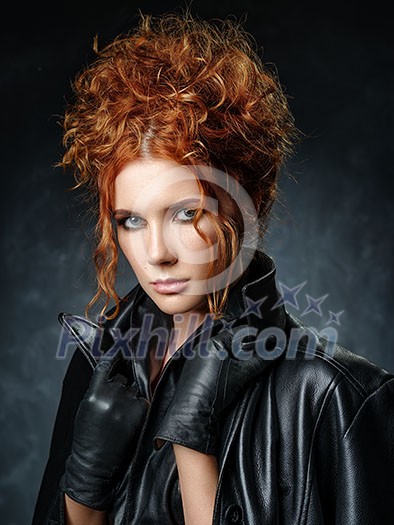 Portrait of red-haired woman in a leather jacket on a dark background. Seductive look at the camera.