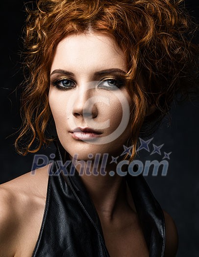 Headshot of red-haired woman in a leather jacket on a dark background. Seductive look at the camera.