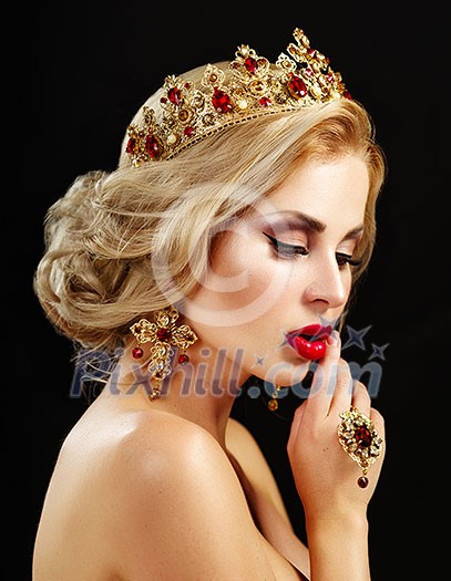 Beautiful blonde girl with a golden crown, earrings and professional evening make-up. Beauty face over black background.