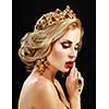 Beautiful blonde girl with a golden crown, earrings and professional evening make-up. Beauty face over black background.