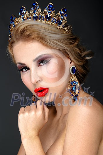 Beautiful blonde girl with a golden crown, earrings and professional evening make-up. Beauty face.