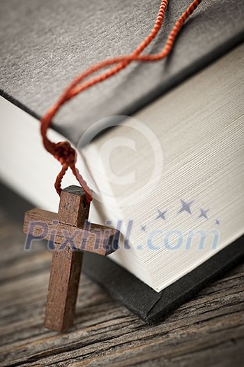 Closeup of wooden Christian cross necklace next to holy Bible Closeup of wooden Christian cross necklace next to holy Bible