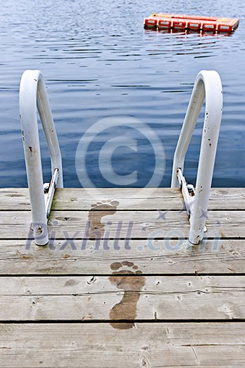 Wet footprints on dock with ladder and diving platform at calm summer lake in Ontario Canada