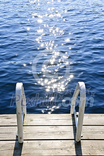 Dock and ladder on calm summer lake with sparkling water in Ontario Canada Dock and ladder on calm summer lake with sparkling water in Ontario Canada
