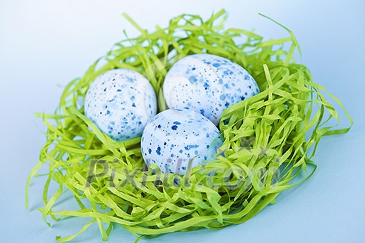Three blue speckled easter eggs in green paper grass nest Three blue speckled easter eggs in green paper grass nest