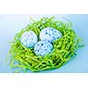 Three blue speckled easter eggs in green paper grass nest