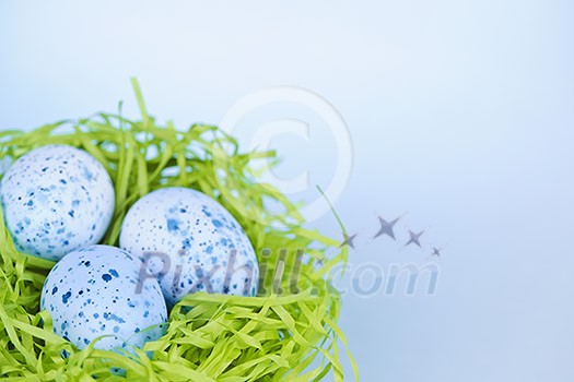 Three blue speckled easter eggs in green paper grass nest with copy space