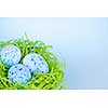 Three blue speckled easter eggs in green paper grass nest with copy space