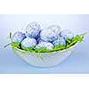 Many blue speckled easter eggs in bowl on green paper grass