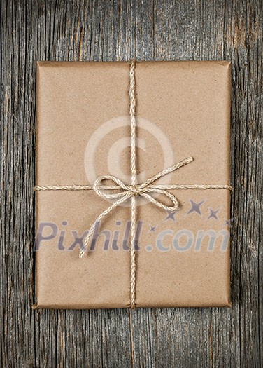 Gift package in brown paper wrapper tied with string on rustic wood background