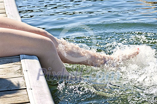 Girl sitting on dock splashing bare legs in lake Girl sitting on dock splashing bare legs in lake