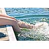 Girl sitting on dock splashing bare legs in lake