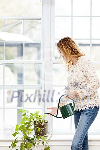 Smiling woman watering green plant at home by window