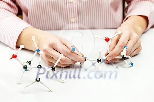 Hand of female student assembling amino acid molecule models for science project