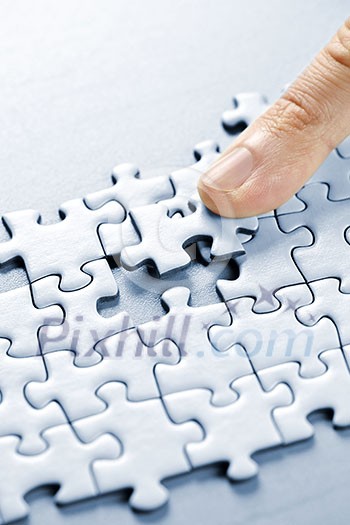 Finger pushing missing puzzle piece into place Finger pushing missing puzzle piece into place