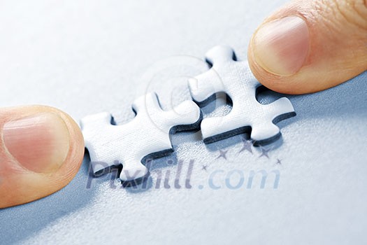 Fingers pushing two matching puzzle pieces together Fingers pushing two matching puzzle pieces together