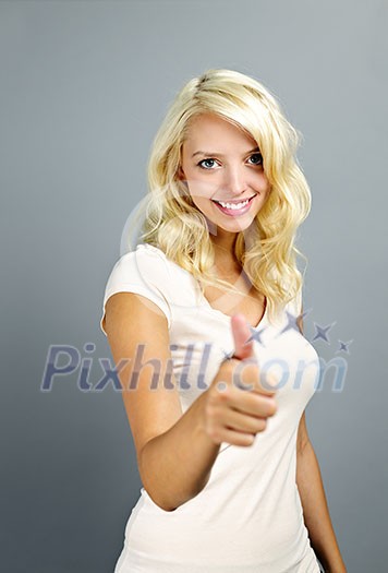 Smiling young blonde woman giving thumbs up on grey background Smiling young blonde woman giving thumbs up on grey background
