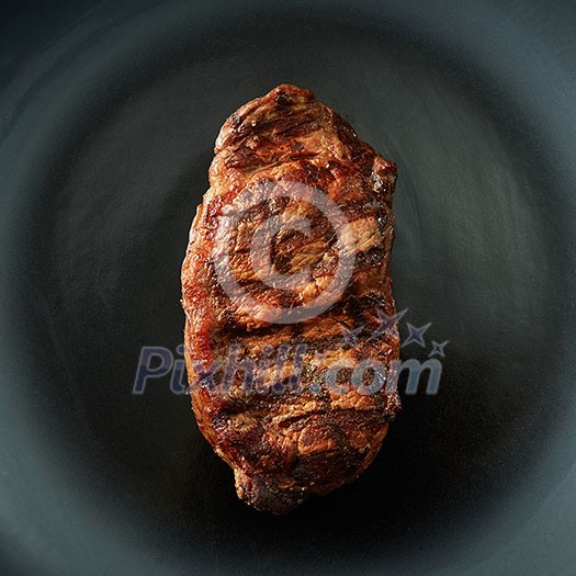 Beef steak served on black plate with fork and knife on dark table Beef steak served on black plate with fork and knife on dark table