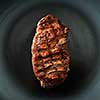 Beef steak served on black plate with fork and knife on dark table