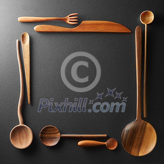 frame of wooden spoons, forks and a knife on black background