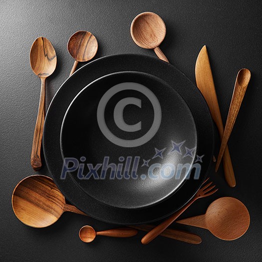 two black plates and wooden spoon, fork, knife on a black table. two black plates and wooden spoon, fork, knife on a black table.