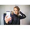 Young woman shopping in a fashion store, trying on some clothes she likes  - taking a selfie picture with her smartphone in the cabin (color toned image; shallow DOF)