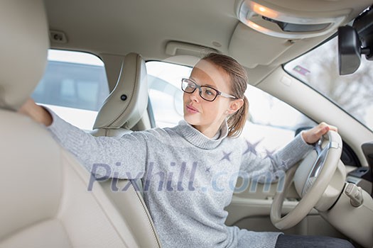 Woman driving a car - female driver at a wheel of a modern car, parking, going in reverse using the parking sensors (DOF; color toned image) Woman driving a car - female driver at a wheel of a modern car, parking, going in reverse using the parking sensors (DOF; color toned image)