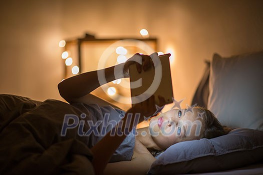 Young woman using her tablet computer in her bed late at night (color toned image; shallow DOF)