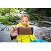 Pretty, young female hiker taking a selfie while outdoors on a hike, taking a break near a mountain stream (shallow DOF)