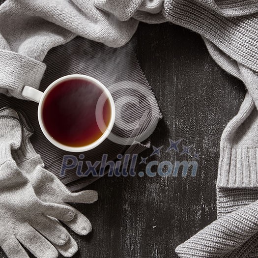 Knitted handmade wool clothing. Autumn or winter clothes and a cup of hot tea cup on a black background.