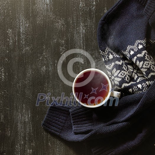 Cozy winter home background, cup of hot tea and warm knitted sweater on black background.