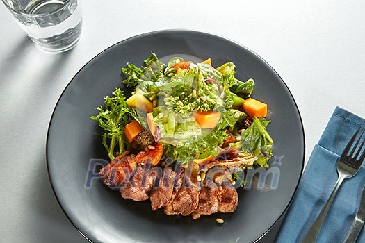 grilled duck meat with roasted pumpkin and fresh green salad on a plate with cutlery on a table grilled duck meat with roasted pumpkin and fresh green salad on a plate with cutlery on a table