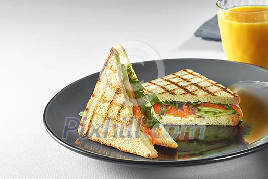 toast sandwich with salmon, vegetable and salad on plate and fresh orange juice toast sandwich with salmon, vegetable and salad on plate and fresh orange juice