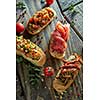 Italian crostini with various toppings on dark wood background, top view