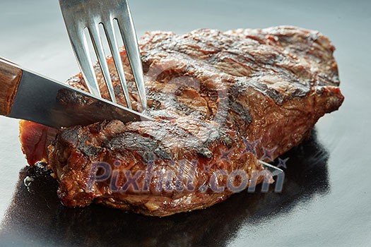 piece of steak cut with a fork and knife on dark background piece of steak cut with a fork and knife on dark background