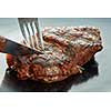 piece of steak cut with a fork and knife on dark background