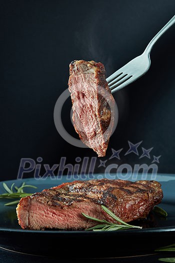 Beef steak medium grilled with rosemary and a piece of meat on a fork Beef steak medium grilled with rosemary and a piece of meat on a fork
